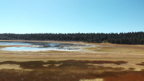 Flying-over-a-grassy-golden-mountain-meadow,-and-a-dried-up-muddy-lake