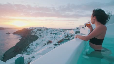 Girl-in-jacuzzi-drinking-from-a-wine-glass,-watching-the-sunset-in-Oia,-Santorini