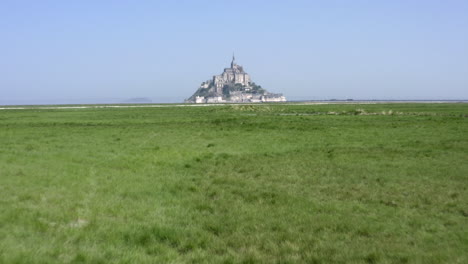Low-altitude-flight-towards-Mont-Saint-Michel-across-green-grass-fields