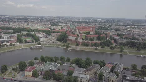 Poland,-Krakow-drone-shot-zooming-in-from-the-front-of-the-Castle-Wawel-with-Wisla-in-foreground-and-buildings-in-the-background