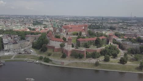 Poland,-Krakow-drone-shot-zooming-in-from-the-front-of-the-Castle-Wawel-with-Wisla-in-foreground-and-buildings-in-the-background
