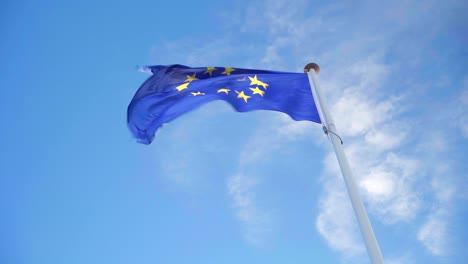 Looking-up-the-EU-flag-waving-on-its-own-in-strong-wind-on-a-blue-and-cloudy-sky,-symbol-of-the-European-Union-alliance