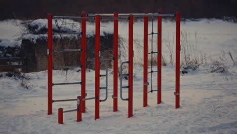 outdoor-gym-with-no-people-at-snowed-park-in-winter,-red-metal-fitness-equipment-empty-in-the-snow,-athletic-urban-lifestyle