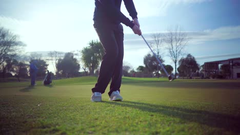 Swing-shot-of-a-golfer-on-the-approach-green-of-a-golf-course,-on-a-sunny-day