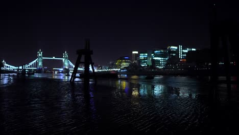 Londoner-Skyline-Bei-Nacht,-Blick-Auf-Die-Tower-Bridge,-Gebäude-Und-Wolkenkratzer-Von-Der-Themse-Bei-Ebbe,-Schöne-Lichtreflexionen-Im-Wasser