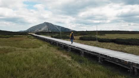 Isolated-Hiker-at-Upa-peat-bog-in-Krkonose-or-Giant-mountains,-Czech-republic-with-Snezka-peak-in-the-distance,-drone-follow,-4k-or-UHD,-30fps
