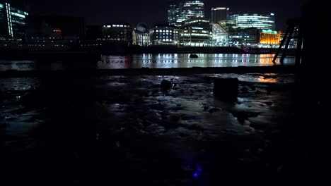 London-skyline-at-night,-The-Shard,-buildings-and-skyscrapers,-view-from-the-river-Thames-at-low-tide,-beautiful-light-reflections-in-the-water