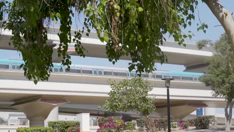 Moderner-Zug,-Der-An-Einem-Sonnigen-Tag-In-Der-Nähe-Des-Al-rashidiya-parks-In-Dubai,-Vae,-über-Die-Von-Baumlaub-überdachte-Eisenbahn-Fährt