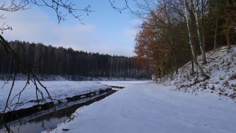 Der-Kleine-Fluss-Fließt-Am-Sonnigen-Wintertag-Mit-Schnee-Langsam-In-Der-Nähe-Des-Waldes-Vorbei