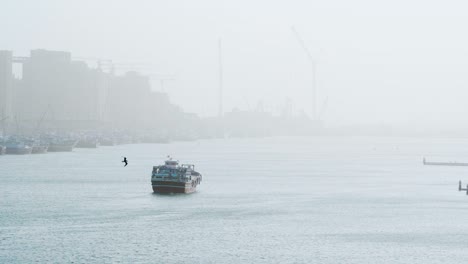 Barco-Flotando-En-Medio-De-Dubai-Creek-Con-Puerto-Deira-En-Un-Fondo-Brumoso