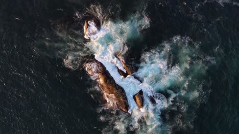 Drone-shot-flying-upwards-looking-down-at-waves-crashing-over-rocks-in-the-ocean