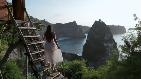 Popular-tourist-tree-house-on-Nusa-Penida-cliff-with-female-traveler-in-white