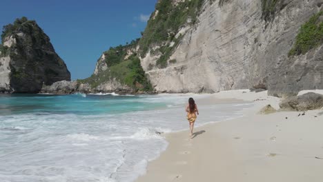 Girl-running-on-tropical-Diamond-beach-with-tall-cliffs-of-Nusa-Penida