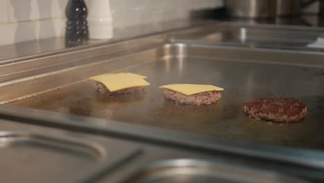 Hands-of-chef-putting-cheese-on-hot-steaming-patties-while-cooking-on-stove
