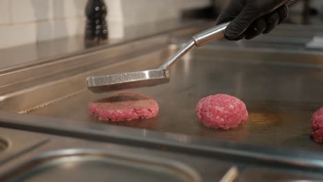 Chef-puts-three-balls-of-minced-meat-on-hot-stove-and-pushes-into-patties,-static-shot