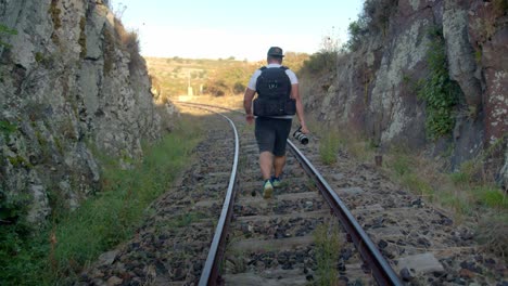 Rising-reveal-of-a-young-man-walking-on-a-railway-track-surrounded-by-rocks