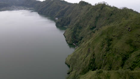 Drone-pan-tilt-up-reveal-of-green-ridge-along-lake-in-Bali