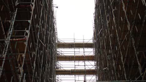 Looking-up-at-high-scaffolding-in-a-building-skyscrapper-under-construction-or-renovation,-on-a-cloudy-day-in-London