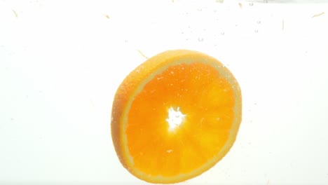 Delicious-slice-of-orange-dropped-into-water-and-floating-up,-close-up-view