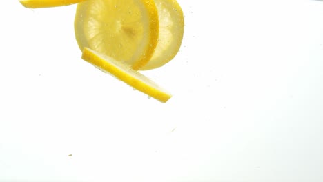 Runde-Zitronenscheiben-Ins-Wasser-Gefallen-Und-Schwimmend,-Isoliert-Auf-Weißem-Hintergrund