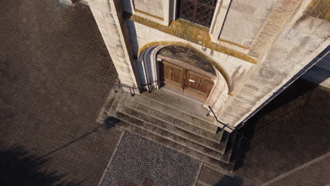 Top-down-rise-aerial-shot-in-front-of-the-doors-of-a-church-in-the-countryside-of-Vionnaz,-Switzerland-on-a-sunny-day