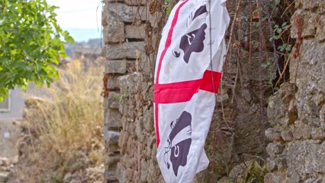 Sardinia-red-and-white-flag-waving-on-side-of-stone-wall,-close-up-handheld-view