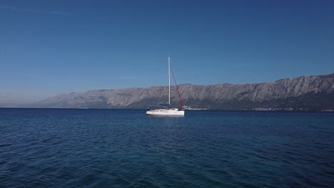 Drone-flying-at-low-altitude-towards-a-sailboat-in-a-open-bay-in-Croatia-with-mountains-in-the-back-flying-over-the-mast
