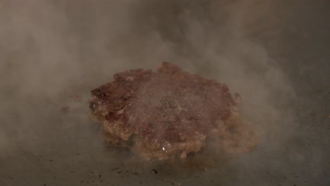 Pressing-hot-juicy-cooking-burger-patty-while-on-stove,-close-up-shot