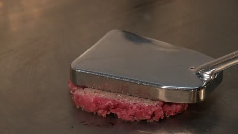 Chef-pressing-ball-of-minced-meat-into-burger-patty-on-hot-stove,-close-up-view