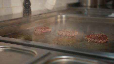 Chef-seasoning-burger-patties-while-cooking-on-hot-stove,-static-shot