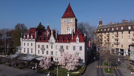 Slow-aerial-orbit-shot-of-a-large-hotel-built-on-the-site-of-an-old-medieval-castle-in-Lausanne,-Switzerland-on-a-sunny-day