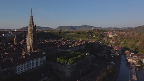 Slow-aerial-shot-above-Bern,-Switzerland-at-sunset-with-a-large-cathedral-in-frame