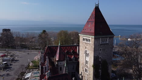 Slow-aerial-fly-over-of-a-large-hotel-built-on-the-site-of-an-old-medieval-castle-in-Lausanne,-Switzerland-with-Lake-Geneva-in-the-background