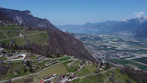 Slow-aerial-shot-of-the-village-of-Torgon,-Switzerland-above-a-farmland-valley-on-a-sunny-day