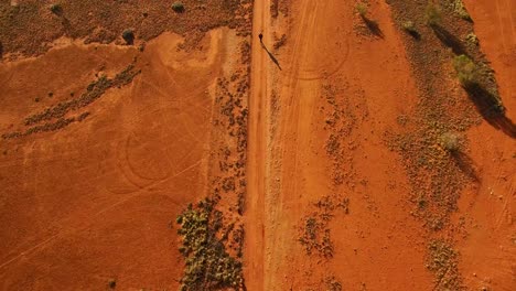 A-person-walks-alone-down-down-a-remote,-red-earth-Australian-outback-road