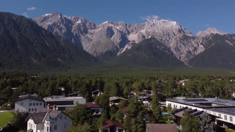 Drone-Rising-up-over-small-village-in-the-Alps-with-massive-Mountains-in-the-back-on-a-sunny-day