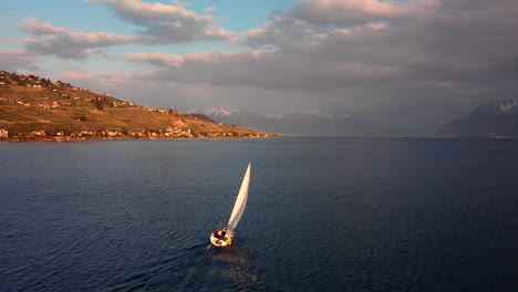 Drone's-flight-over-the-Leman-Lake-from-Vevey,-featuring-the-sailing-boat-going-to-the-French-border-and-aiming-at-the-mountains