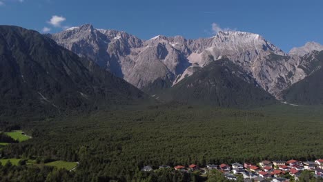 Drone-flying-sideways-to-the-right-along-a-massive-Alp-mountain-side-view-with-woods-and-houses-in-Europe