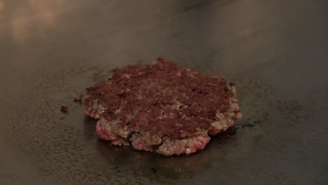 Chef-flipping-burger-patty-with-spatula-in-hot-cooking-stove,-close-up-shot