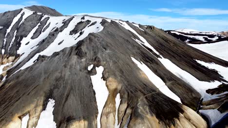 Aerial-pull-out-above-couloir-filled-with-snow-on-rainbow-mountains-of-Landmannalaugar-in-Iceland