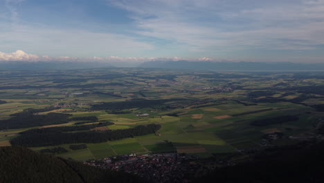 Expansive-aerial-view-high-above-the-countryside-of-Sainte-Croix,-Switzerland-with-the-Swiss-Alps-in-the-distance