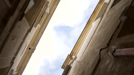 POV-shot-looking-up-between-two-old-stone-buildings-in-a-street-a-South-of-France-village,-on-a-beautiful-day-with-blue-sky,-spinning-and-vertigo-effect