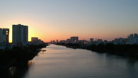 Cinematic-Sunset-Drone-shot-flying-over-canal-to-sunflare-Ho-Chi-Minh-City,-Vietnam