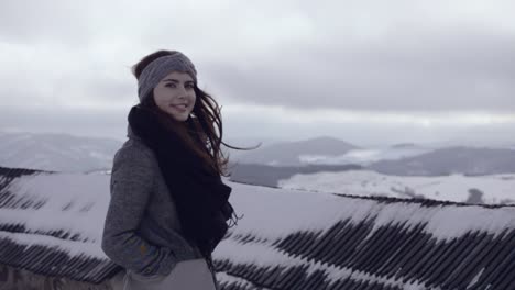 Girl-in-the-grey-coat-and-black-scarf-standing-in-the-cold-winter-wind-and-enjoying-snowy-scenery-in-the-distance,-50p