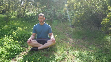 Ein-Mann,-Der-In-Einer-Meditationspose-Auf-Einer-Grünen,-Sonnigen-Waldwiese-Sitzt-Und-Tiefe-Atemübungen-Praktiziert,-Um-Stress-Abzubauen-Und-Die-Geistige-Gesundheit-In-Zeitlupe-Zu-Steigern