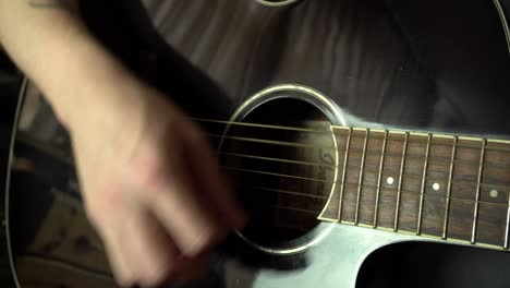 Close-up-of-a-young-man-with-tattoo-strumming-acoustic-guitar