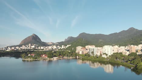 Seitliche-Luftbewegung,-Die-Den-Stadtsee-Rio-De-Janeiro-Bei-Sonnenaufgang-Zur-Blauen-Stunde-Zeigt,-Der-Die-Landschaft-In-Der-Oberfläche-Des-Ruhigen-Wassers-Darunter-Widerspiegelt