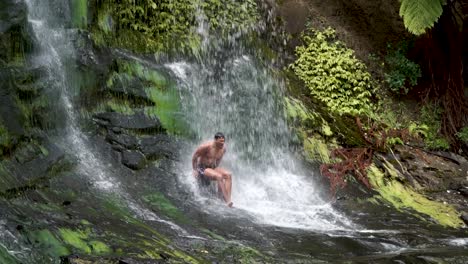 Slowmo---Joven-Sentado-Bajo-Mokoroa-Falls,-Auckland,-Nueva-Zelanda