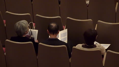 Three-asian-spectators-sitting-at-a-concert-hall-with-a-program-in-their-hands