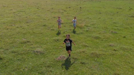 Children-run-and-play-in-green-field---aerial-tracking-shot